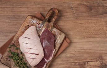 Fresh raw duck breasts, on a wooden chopping board, with herbs and spices, no people