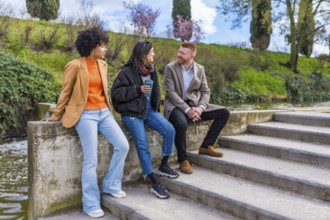 Three young professionals enjoying a conversation and coffee by a canal after work, representing