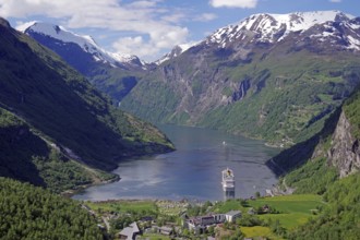 A fjord with a cruise ship surrounded by green mountains with snow-capped peaks under a blue sky