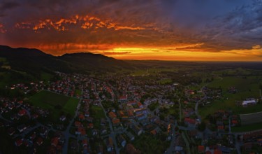 A village under a dramatic sunset sky with glowing clouds and mountains in the background, Bad