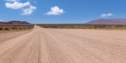 An endless desert road under a blue sky with a wide, dry landscape and mountains in the background,