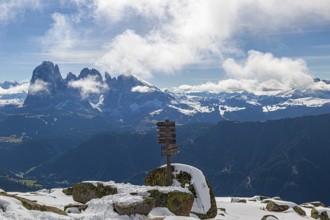 Snow-covered mountains under a blue sky with clouds and a wooden signpost with a view of the