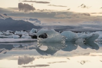 Icebergs reflected in calm water against a mountain backdrop, clouds, Jökulsárlón glacier lagoon or