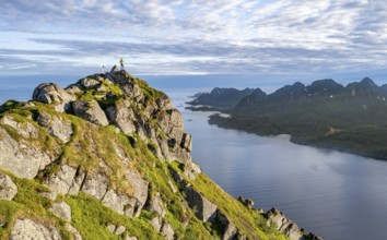 Climber on the summit of Dronningsvarden or Stortinden, behind sea and fjord Umvågsundet,
