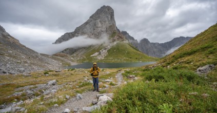 Mountaineers on a hiking trail with a view of rocky cloudy mountains and Wolayersee, hiking trail