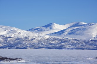 Snow-capped mountains and a frozen lake under a clear blue sky, Abisko, Abisko National Park,
