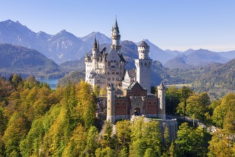 Neuschwanstein Castle against an alpine backdrop with colourful autumn vegetation and a clear sky,