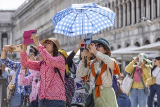 Tourists from Asia with mobile phones and parasols taking photos. Souvenir photo of St Mark's