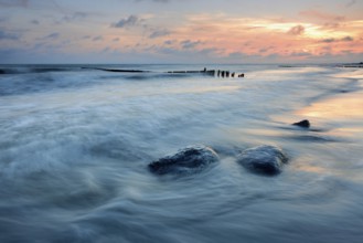 Sunset on the beach, boulders and old groyne in the surf, Klintholm Havn, Møn Island, Denmark,