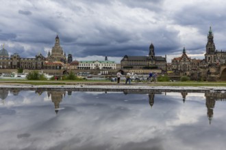 The Dresden silhouette with dark clouds behind the Church of Our Lady is reflected in a puddle on