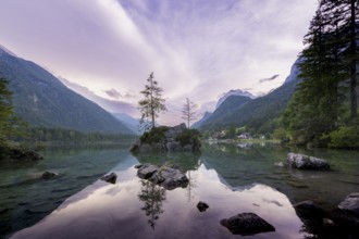 Hintersee with rocks and trees in the foreground, surrounded by mountains after sunset with