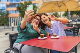 Cheerful disabled woman and asian female friend gesturing success taking selfie sitting in an