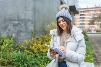Young woman writing on notebook sitting on a bench in winter in the city