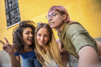 Diverse young women gesturing success while taking selfie together in the city