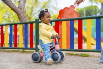 Full length photo of a cute african baby girl riding a toy bike in a park