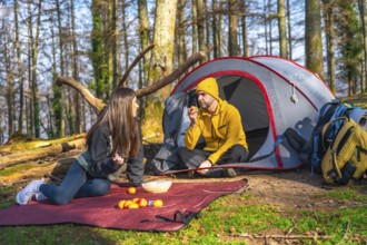 Couple of hikers having a snack next to their tent during a camping trip in the forest, enjoying