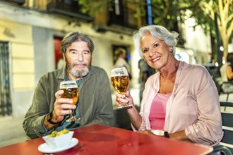 Senior couple toasting at camera with beer in outdoor terrace in the city street