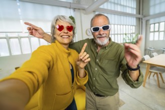 Frontal personal point of view of a happy senior couple with fun sunglasses taking selfie at