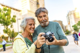 Senior modern caucasian couple looking at the images on a camera screen while visiting a city