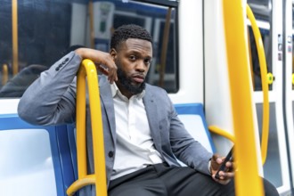 Young businessman engaging with smartphone while commuting on subway train, navigating messages and