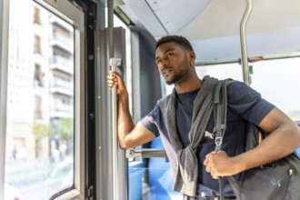 African casual businessman standing on a public bus looking through the window in the city