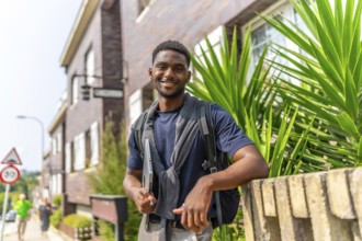 Portrait of a confident african entrepreneur holding laptop standing next to a house in a