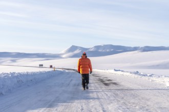 A man walking along a frozen road in the cold winter of Iceland