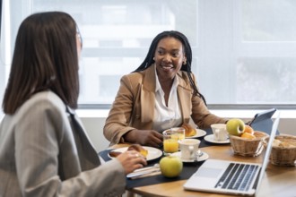 Two businesswomen enjoying breakfast and engaging in conversation during their business trip,