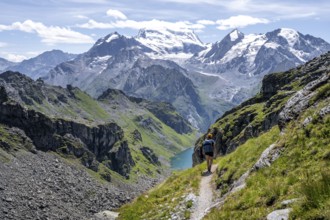 Hiker on hiking trail, mountain lake Lac de Louvie with glaciated summit of the Grand Combin, Val