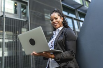 Modern latin businesswoman with long braids working using laptop standing outside a financial