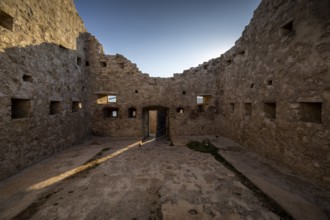Stone ruin with sunlight through the entrance, surrounded by historic walls, Pag, Croatia, Europe