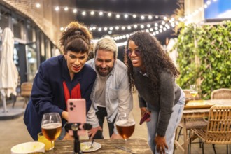 Diverse friends using phone making video call during night party in a bar terrace outdoors