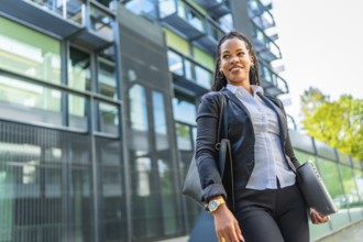 Confident cuban businesswoman walking out the block office carrying handbag and laptop
