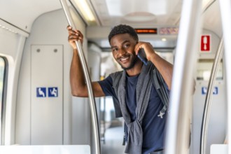Cheerful African young businessman smiling while talking to the mobile travelling by metro