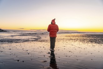 A man in an orange jacket walking at sunrise on Diamond Beach Iceland in winter