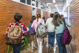 Group of students walking down school hallway between classes, carrying backpacks and rushing to