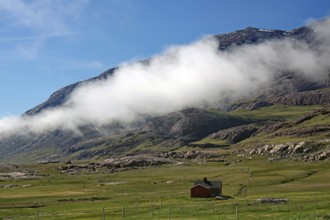 House in a green meadow with mountains and clouds above, blue sky, Igaliku, North America,