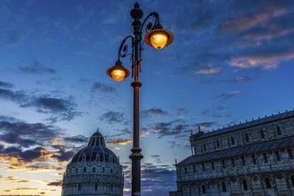 Baptistery and the Cathedral of Santa Maria Assunta at sunset under an illuminated street lamp,