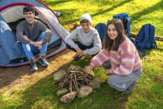 Caucasian father and two sons preparing a bonfire with dry branches in the forest next to camping
