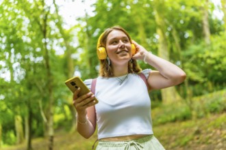 Caucasian young woman listening to music smiling looking up while standing in a footpath in the
