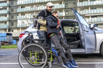 Caregiver lifting a disabled young man from his wheelchair and helping him to get into a car parked