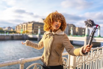 Latin female travel vlogger talking to her audience streaming online next to the river
