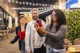 Happy multi-ethnic friends using phone to take a selfie during night outdoor party
