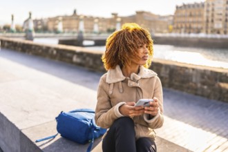 Latin beauty woman using phone sitting in the city next to the river