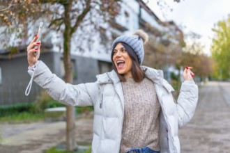 Happy cauacsian young woman smiling during video call with mobile in the street