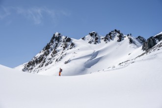 Ski tourer on the descent, minimalist winter landscape, white snow and dark mountains on the