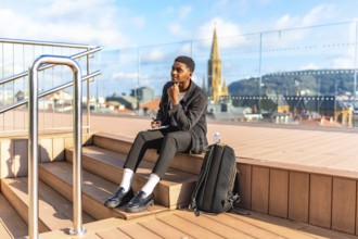 Pensive african young male traveler writing notes sitting on a city viewpoint during sunny day