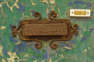 Close-up, old shabby dilapidated front door with antiquated rusty mail slot and yellowed doorbell