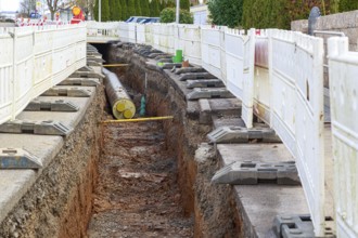 Construction site scene with district heating pipeline in a deep trench and white barriers