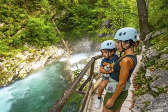 Mother carrying her son while observing stunning turquoise radovna river rapids flowing through